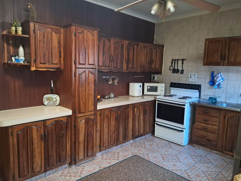 A functional kitchen featuring traditional wooden cabinetry, laminate countertops, tiled backsplash, and a freestanding stove, offering a classic aesthetic with potential for modernization.