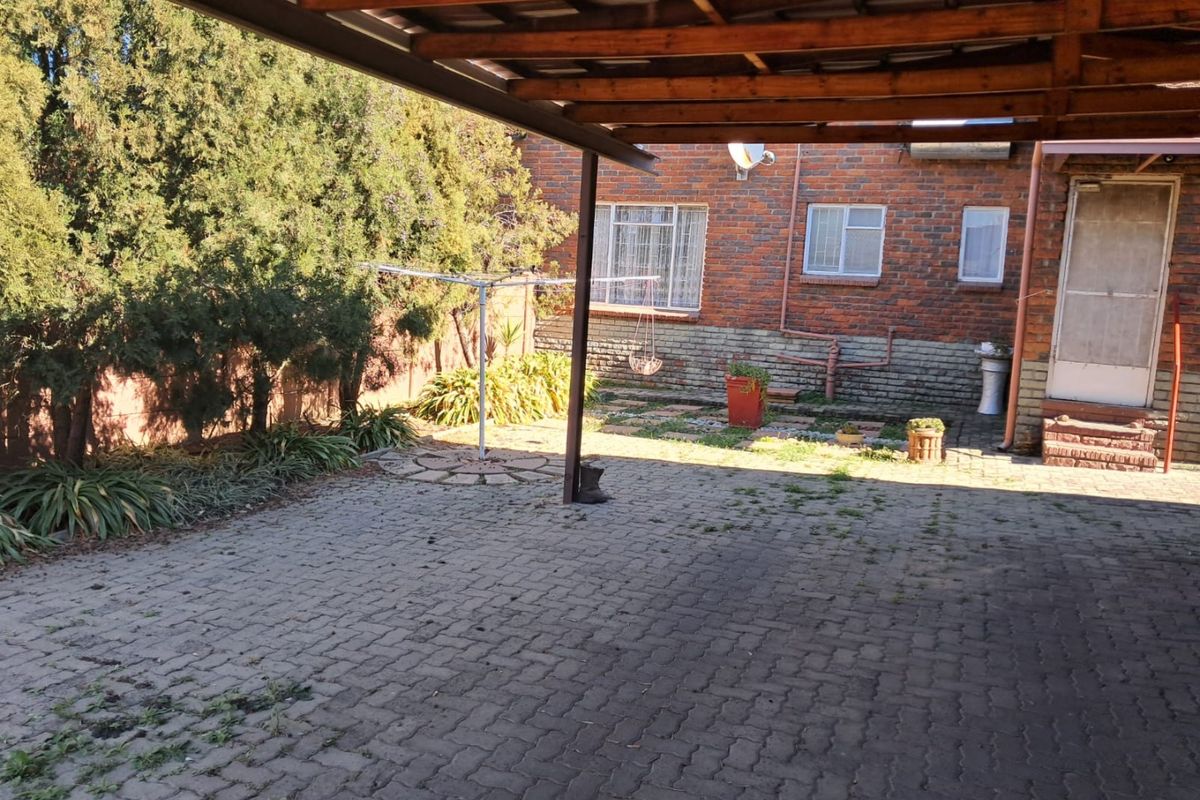 Rear exterior view featuring a paved area, timber pergola, and brick building facade with security features.