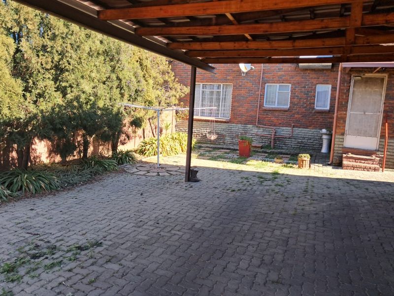 Rear exterior view featuring a paved area, timber pergola, and brick building facade with security features.