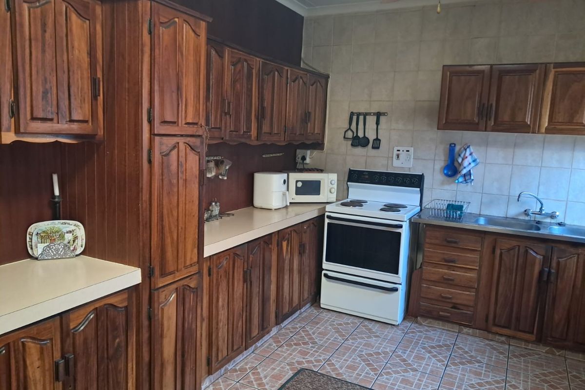 A functional kitchen featuring traditional wooden cabinetry, laminate countertops, a tiled backsplash, and a freestanding stove with ample storage space.