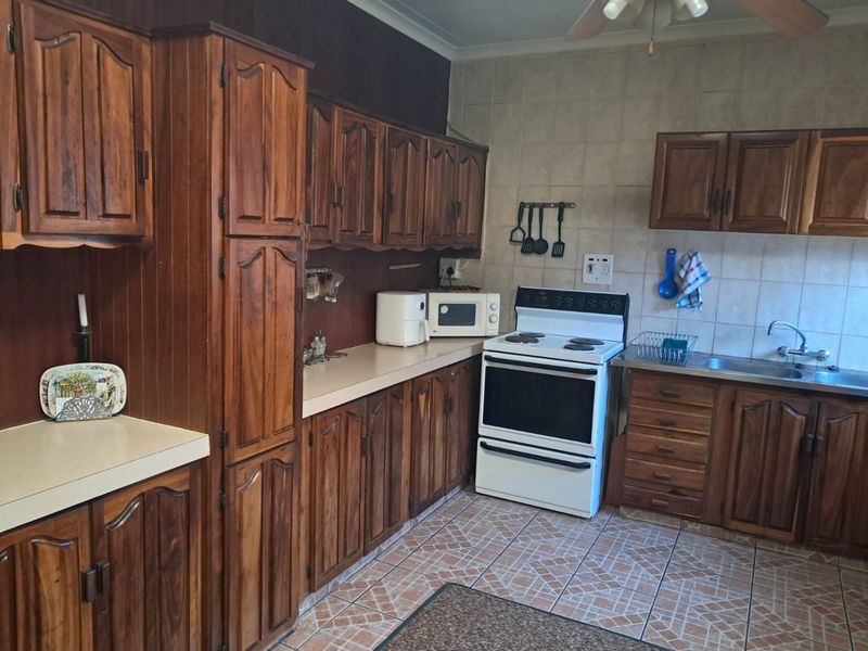 A functional kitchen featuring traditional wooden cabinetry, laminate countertops, a tiled backsplash, and a freestanding stove with ample storage space.