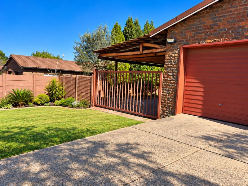 Front exterior view featuring a brick facade, roll-up garage door, concrete driveway, and a private garden area with a carport and boundary wall.