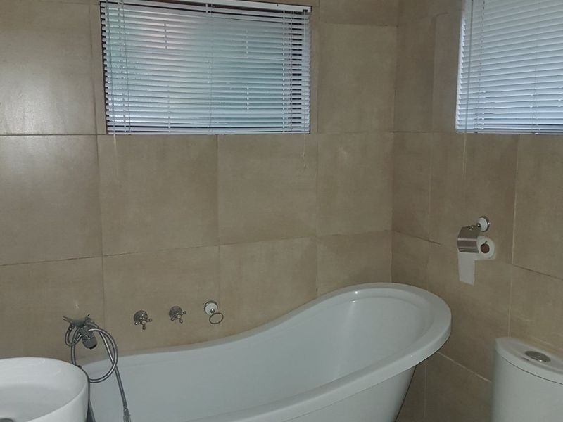 A well-appointed bathroom featuring a classic clawfoot bathtub, vessel sink, ceramic toilet, and neutral wall tiling with integrated venetian blinds.