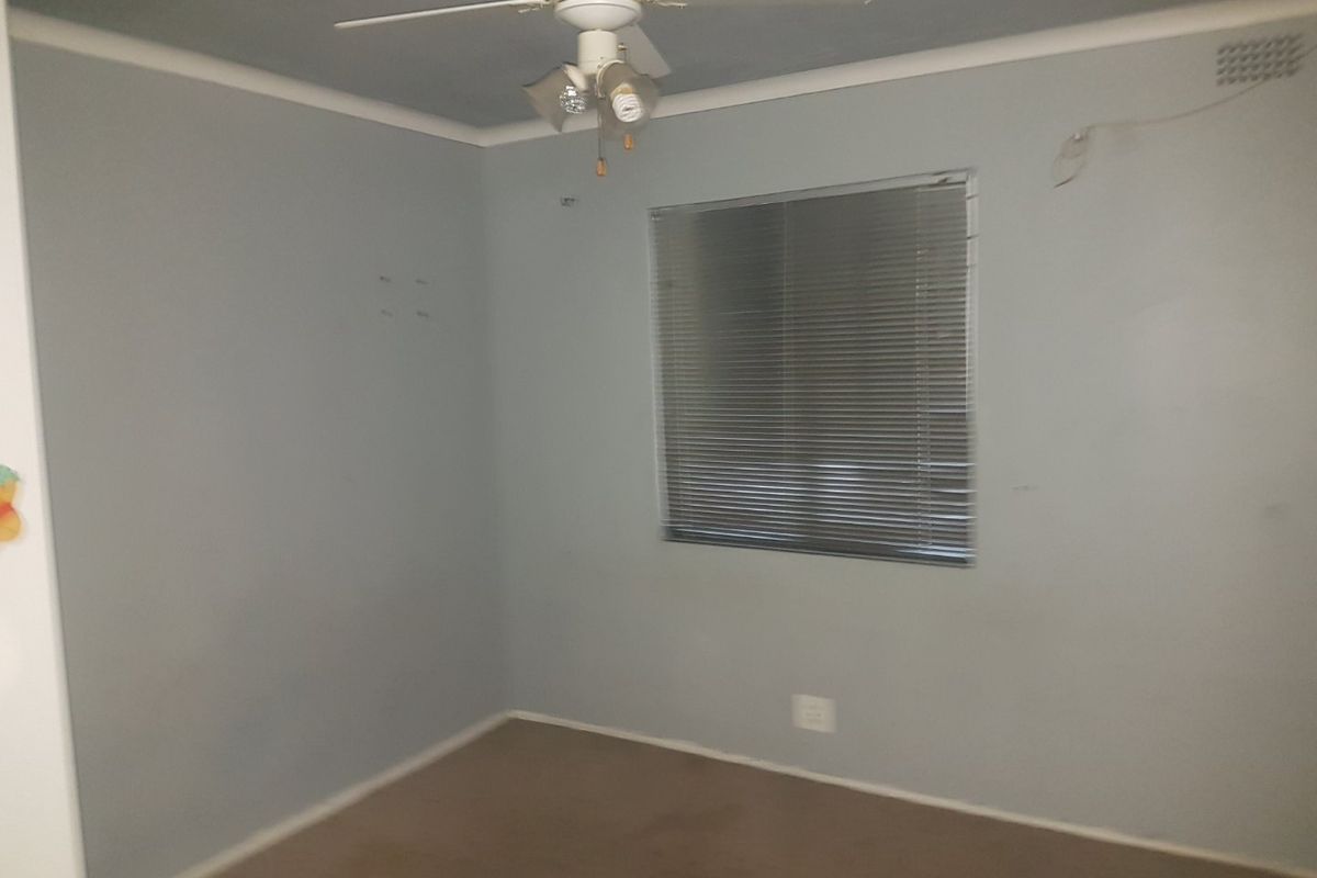 An empty bedroom featuring carpet flooring, a ceiling fan, and venetian blinds. The room requires minor cosmetic updates to the walls and electrical fixtures.
