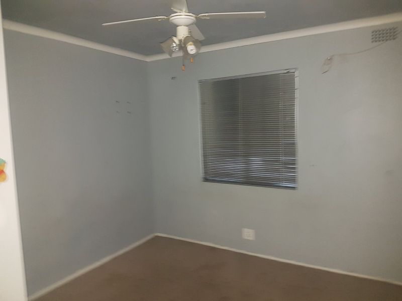 An empty bedroom featuring carpet flooring, a ceiling fan, and venetian blinds. The room requires minor cosmetic updates to the walls and electrical fixtures.
