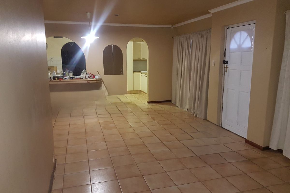 An open-plan living area featuring tiled flooring, an arched entryway to the kitchen, and a breakfast bar, offering a functional layout for renovation.