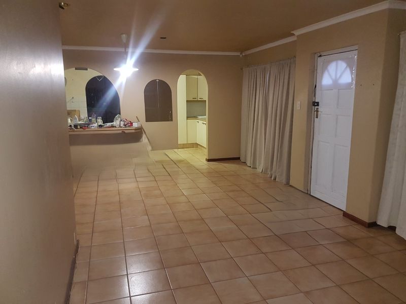 An open-plan living area featuring tiled flooring, an arched entryway to the kitchen, and a breakfast bar, offering a functional layout for renovation.