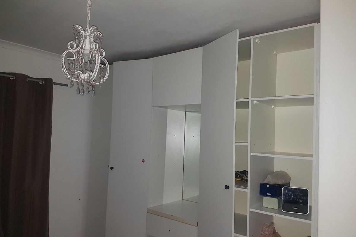 A bedroom featuring a white built-in wardrobe unit with an integrated vanity mirror and shelving, complemented by a decorative pendant light fixture.