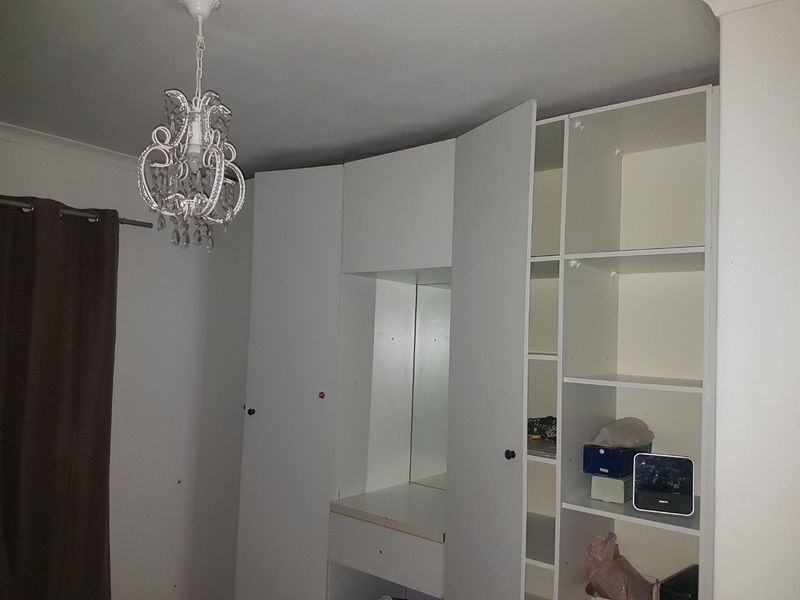 A bedroom featuring a white built-in wardrobe unit with an integrated vanity mirror and shelving, complemented by a decorative pendant light fixture.
