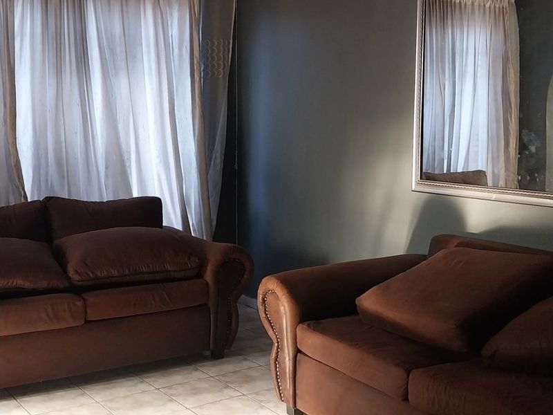 A living room featuring tiled flooring and a tiled ceiling, with dark painted walls and natural light filtering through window curtains.