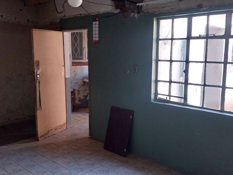 An empty living area featuring tiled flooring and steel-framed windows, currently requiring significant cosmetic renovation and wall repairs.