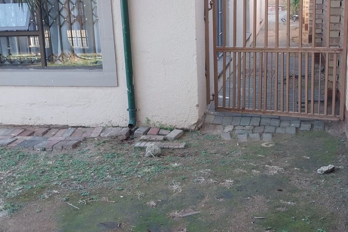 Side exterior view of the property featuring a security gate, razor wire fencing, and paved access path with visible wear to the surrounding ground.