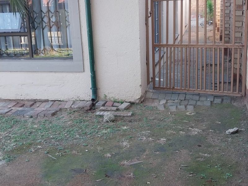 Side exterior view of the property featuring a security gate, razor wire fencing, and paved access path with visible wear to the surrounding ground.