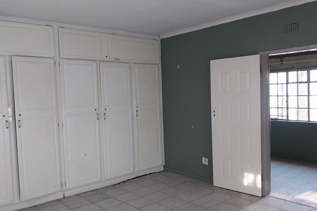 An empty bedroom featuring built-in cupboards, tiled flooring, and a doorway leading to an adjacent space with steel-framed windows.