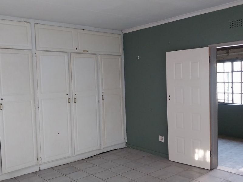 An empty bedroom featuring built-in cupboards, tiled flooring, and a doorway leading to an adjacent space with steel-framed windows.