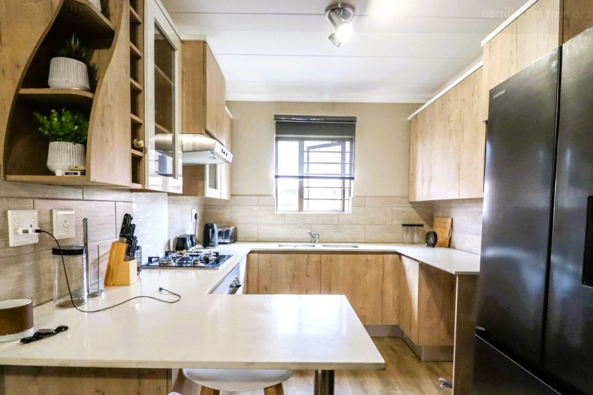 Modern kitchen featuring light wood-finish cabinetry, stone countertops, a gas hob with extractor, and a tiled backsplash with a functional window.