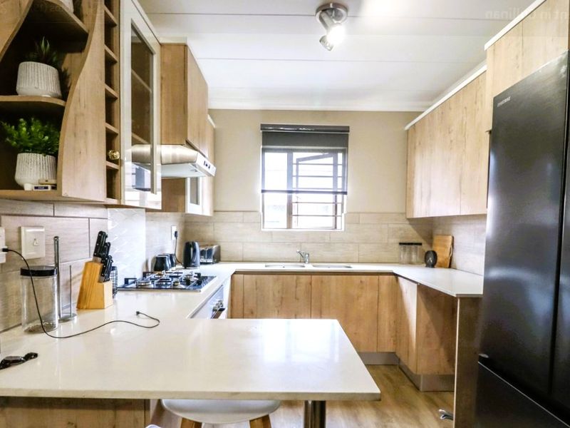 Modern kitchen featuring light wood-finish cabinetry, stone countertops, a gas hob with extractor, and a tiled backsplash with a functional window.