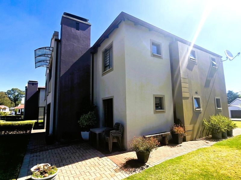 Rear view of the apartment building featuring a paved patio area, chimney stack, and established garden surroundings.