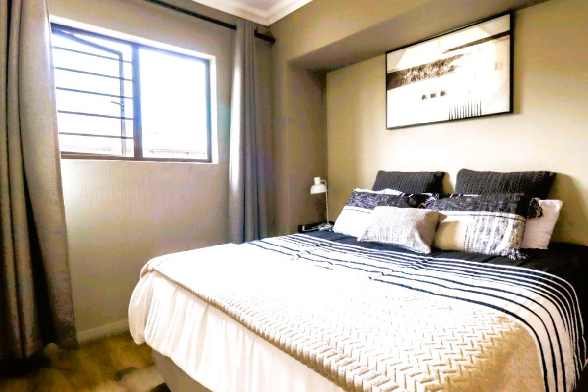 A well-maintained bedroom featuring laminate flooring, coving, and a window fitted with security bars.