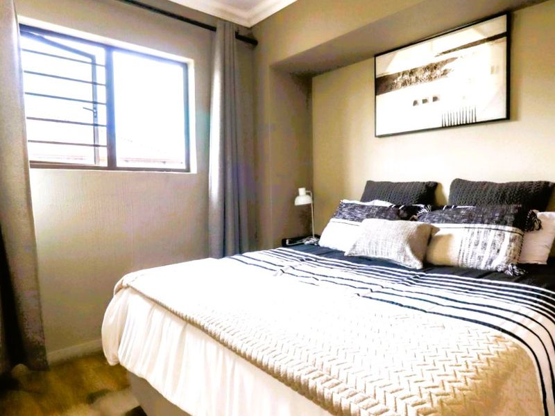 A well-maintained bedroom featuring laminate flooring, coving, and a window fitted with security bars.