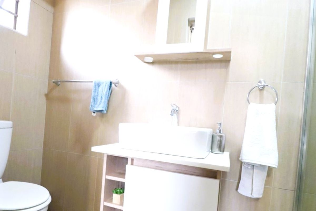A modern bathroom featuring a vessel sink vanity, wall-mounted mirror, toilet, and a glass-enclosed shower with neutral wall tiling.