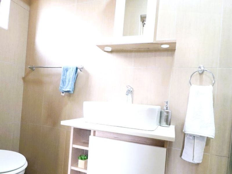 A modern bathroom featuring a vessel sink vanity, wall-mounted mirror, toilet, and a glass-enclosed shower with neutral wall tiling.