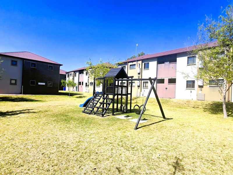 A view of the communal garden area featuring a playground set situated between multi-story apartment buildings.