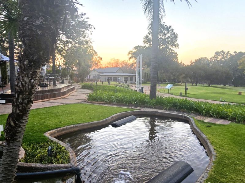 A scenic outdoor area featuring a landscaped garden, a decorative water feature, and wooden decking overlooking a golf course at sunset.