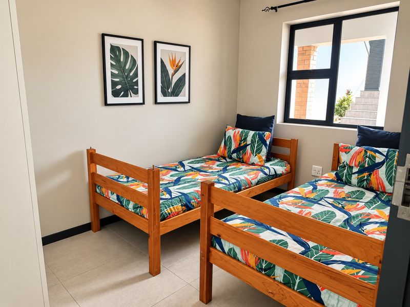 A well-maintained bedroom featuring neutral tiled flooring, a modern black aluminium window frame, and built-in storage space.