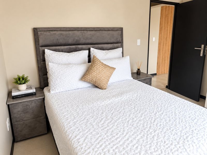 A well-maintained bedroom featuring neutral wall tones, tiled flooring, and a modern dark door leading to an adjacent space.