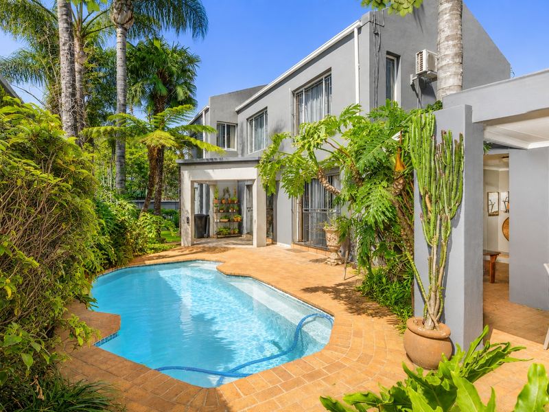 A well-maintained rear garden area featuring a swimming pool, brick-paved surround, and a covered patio area adjacent to the main house structure.