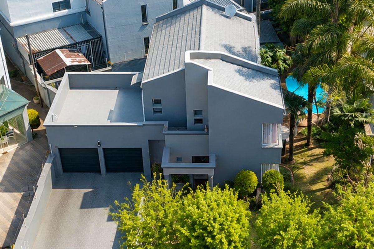 Aerial view of a modern grey house featuring a double garage, paved driveway, perimeter wall, and a private swimming pool in the garden.