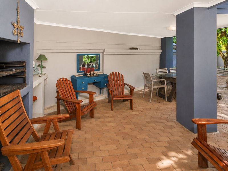 A covered outdoor patio area featuring a built-in braai, paved flooring, and structural columns, providing a functional space for outdoor entertaining.