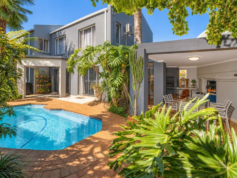A well-maintained outdoor entertainment area featuring a swimming pool, brick-paved surround, and a covered patio with a built-in braai.