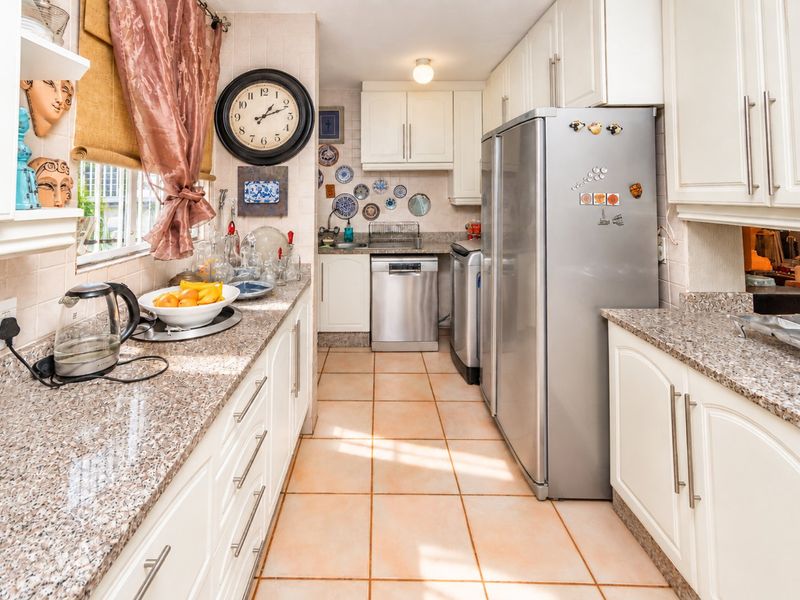 A functional galley-style kitchen featuring granite countertops, ample built-in cabinetry, tiled flooring, and a tiled backsplash.