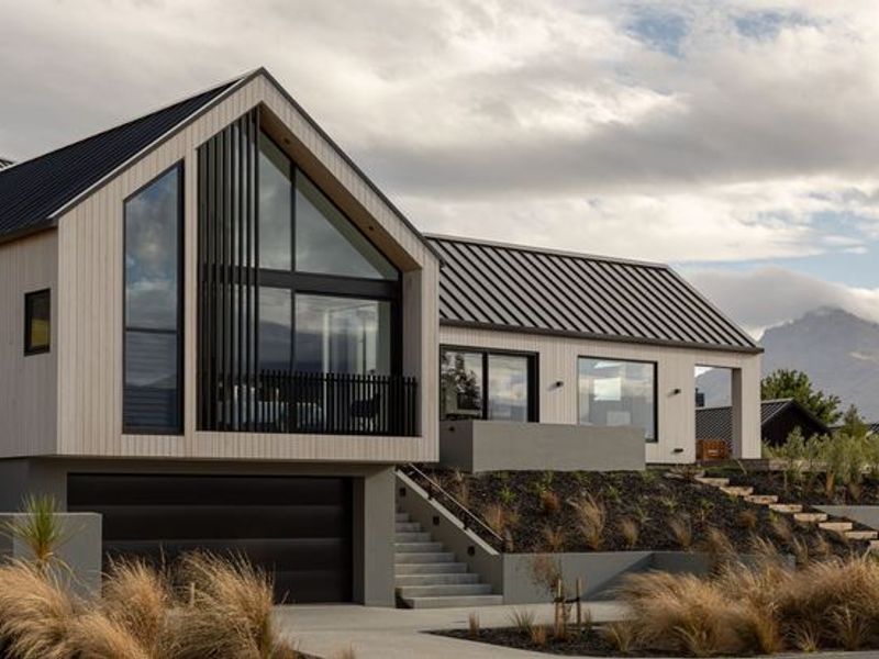 Modern architectural home featuring a striking gabled roof, vertical timber cladding, integrated double garage, and elevated balcony with scenic mountain views.