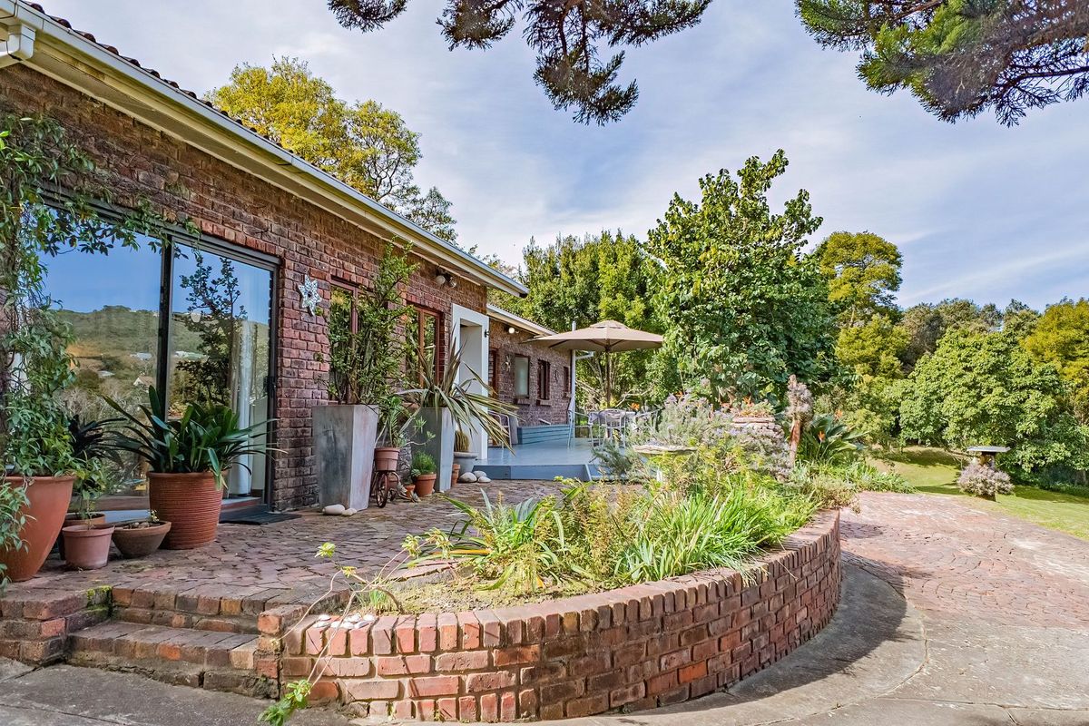A charming rear exterior view featuring a brick facade, sliding glass doors, and a curved brick retaining wall leading to a paved patio area.