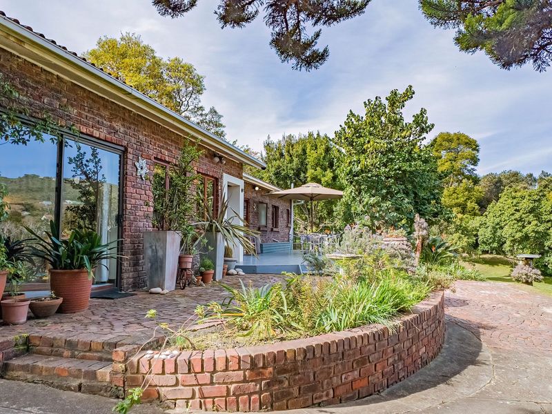 A charming rear exterior view featuring a brick facade, sliding glass doors, and a curved brick retaining wall leading to a paved patio area.
