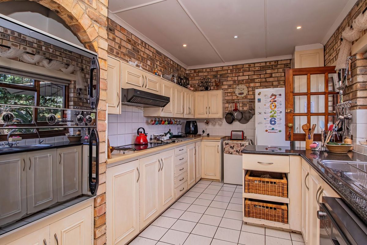 A functional kitchen featuring exposed brick walls, fitted cabinetry, granite countertops, a built-in oven, and a double sink with tiled flooring.
