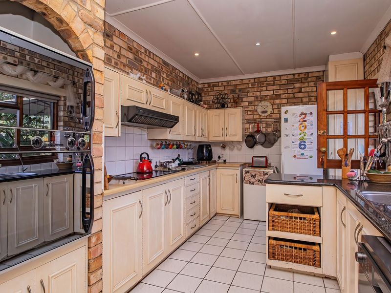 A functional kitchen featuring exposed brick walls, fitted cabinetry, granite countertops, a built-in oven, and a double sink with tiled flooring.