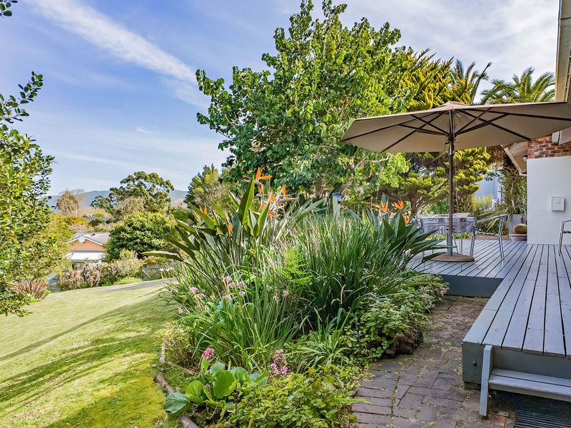 A well-maintained timber deck patio overlooking a lush landscaped garden with mature trees and scenic views.