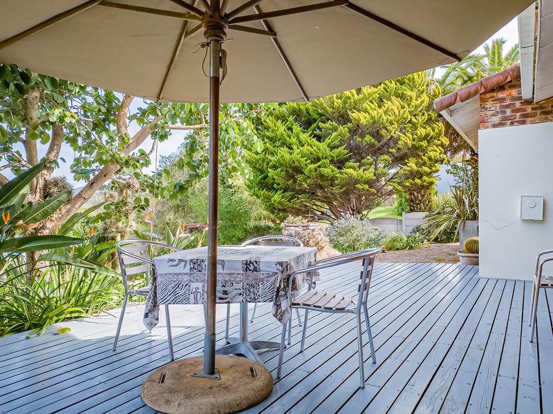 A covered timber deck patio area featuring brick wall accents and direct access to a lush, established garden setting.