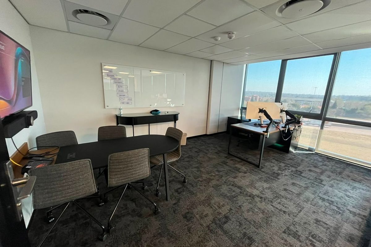 A modern commercial office space featuring carpeted flooring, a suspended ceiling with recessed lighting, and large windows providing natural light and exterior views.