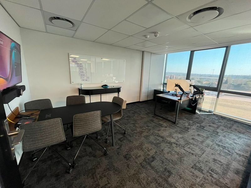 A modern commercial office space featuring carpeted flooring, a suspended ceiling with recessed lighting, and large windows providing natural light and exterior views.