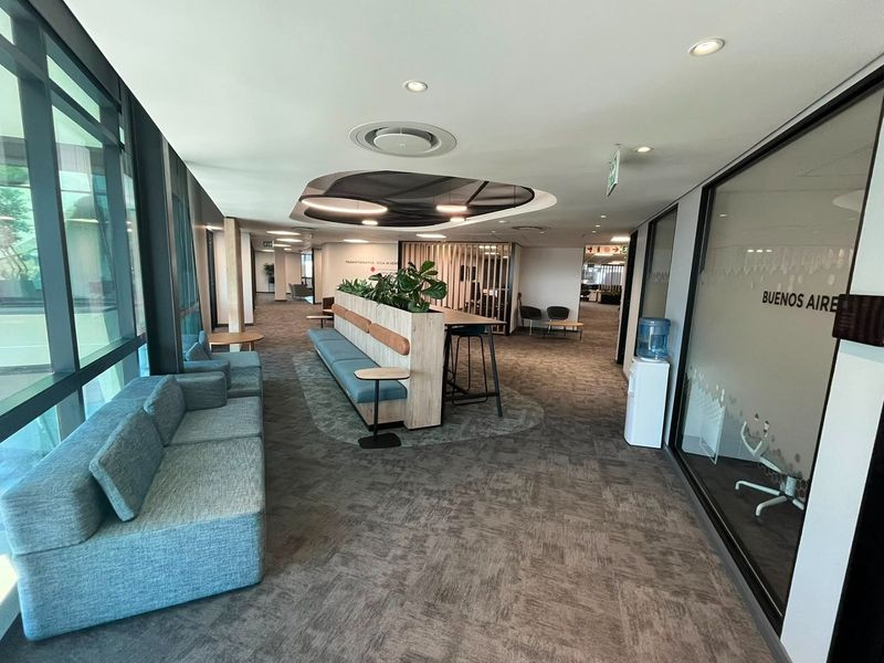 Modern open-plan commercial office space featuring glass partitions, recessed ceiling lighting, and integrated seating areas with carpeted flooring.