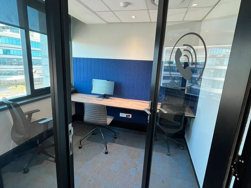 A modern, compact private office pod featuring acoustic wall paneling, a built-in desk, and a glass entry door, ideal for focused work or calls.