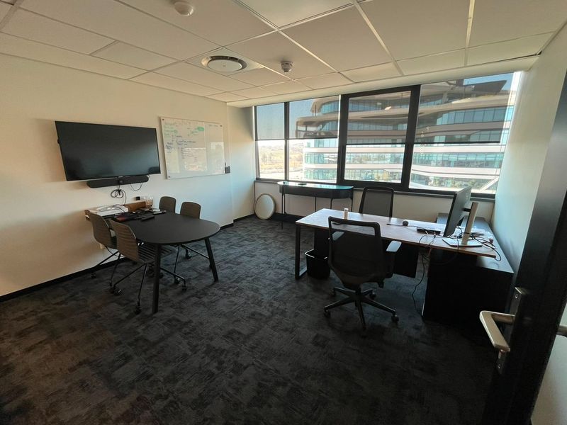 A professional office space featuring a suspended ceiling, large windows with natural light, and carpeted flooring, suitable for a corporate work environment.