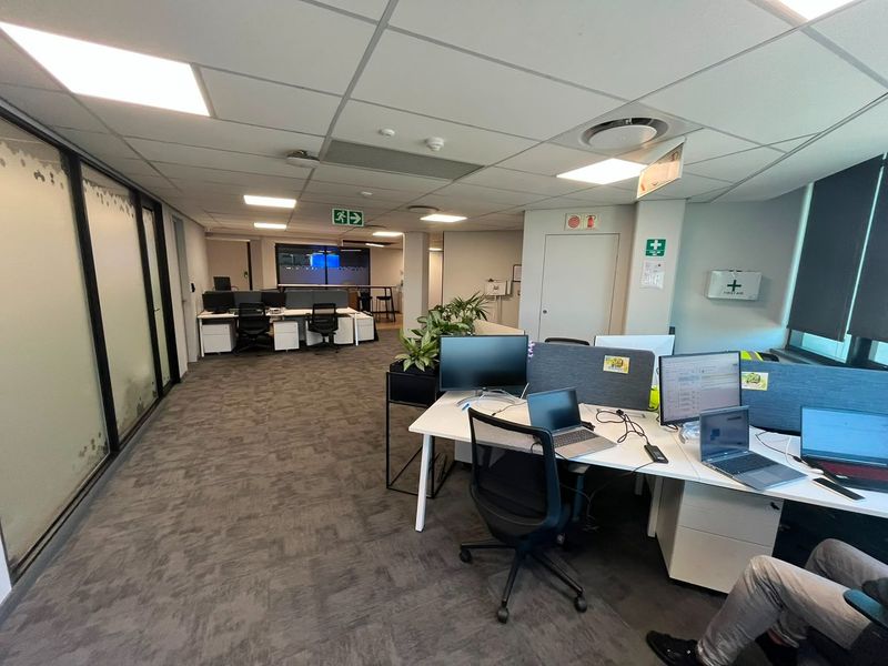 A functional open-plan commercial office space featuring suspended ceilings, recessed lighting, carpeted flooring, and glass partition walls.
