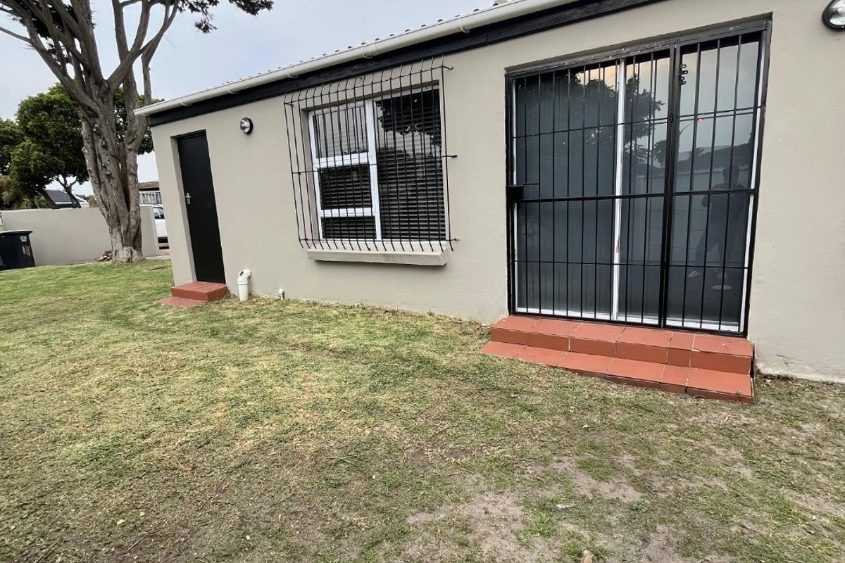 Rear exterior view of the house featuring a sliding door with security bars, tiled steps, and a lawn area.