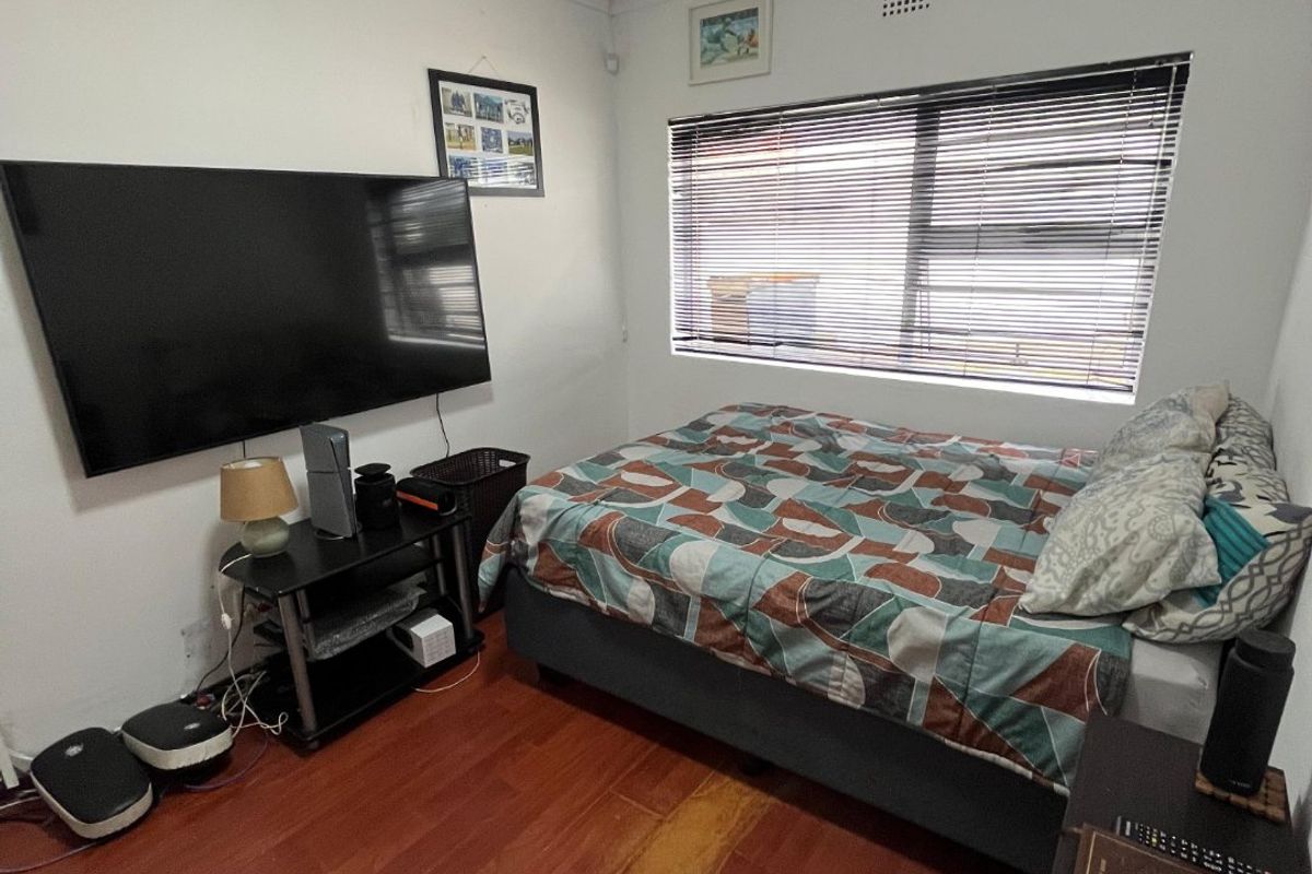 A functional bedroom featuring laminate flooring, a window with venetian blinds, and ceiling cornice detailing.